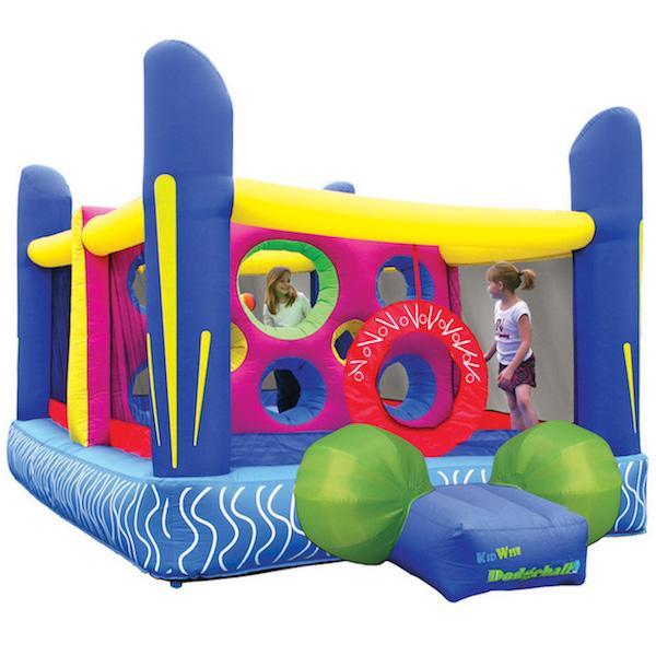 KidWise Jump'n Dodgeball Sports Bounce House display image on white background.  Blue base with 4 big blue inflated support post in each corner.  Yellow cross bar connects the supports.  Green balls adorn the side of the entry ramp.  You can also see the middle partition with round spaces for throwing and climbing, it is violet.  Kids are also playing inside.